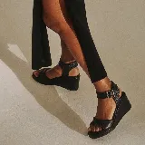 Sandalias de plataforma tipo cuña, color marrón, con tiras de cuero texturizado y costuras decorativas. Cuentan con tira al tobillo con hebilla metálica y plataforma corrida.