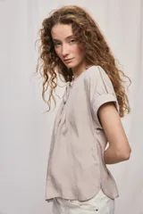 Camisa de manga corta color celeste, confeccionada en viscosa fluida, con silueta amplia y escote redondo con frunces y lazo para anudar.