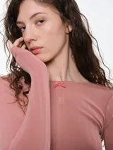 Remera de manga larga entallada confeccionada en tejido pointelle suave, con escote a la base y detalle de pequeño lazo decorativo en el centro. Presenta terminaciones con borde picot.