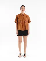 Camisa de manga corta color amarillo claro, con calce oversized, hombros caídos y cierre frontal con botones. Cuenta con bolsillos delanteros con bordados geométricos y mangas con dobladillo.