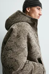 Cazadora acolchada de corte relajado con estampado jacquard. Presenta cuello subido con capucha, cierre frontal de cremallera, bolsillos frontales y puños con acabado elástico.