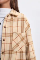 Sobrecamisa de corte holgado con diseño de cuadros en tonos beige y rosado, cuello camisero, cierre frontal con botones y bolsillos delanteros en el pecho.
