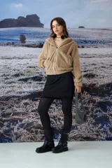 Chaqueta tipo teddy de textura suave y peluda, color beige, con capucha, cierre frontal completo y bolsillos laterales.