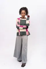 Buzo de tejido de punto con diseño geométrico de cuadros en tonos verde oscuro, rosa y crema. Presenta cuello redondo, puños y ruedo en color bordó, con mangas largas y corte holgado.