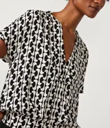 Blusa de viscosa con estampado geométrico en blanco y negro, escote de pico, manga corta y bajo elástico.