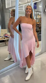 Vestido largo rosado con brillo, strapless y diseño asimétrico con volados en la parte inferior.