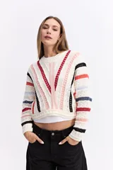 Buzo de tejido calado con diseño de rayas horizontales y verticales en colores blanco, rojo, negro y rosa. Presenta cuello redondo, mangas largas y un corte corto tipo crop.