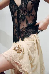 Falda corta de tiro bajo confeccionada en tul color beige, con capas, bajo asimétrico, bordados florales oscuros con lentejuelas en contraste y cierre lateral con nudo.