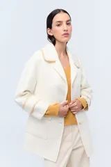 Tapado color crema con cuello solapa, cierre con botones y bolsillos laterales. Presenta detalle de costuras en contraste en cuello, puños y solapa.