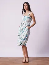 Vestido midi blanco con estampado floral celeste y verde, escote recto con tirantes, abertura frontal con botones, lazo en la cintura y bolsillos laterales.