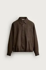 Cazadora de corte relajado color marrón, confeccionada en tejido de algodón. Presenta cuello solapa, cierre frontal con botones, bolsillo plastrón en el pecho, bolsillos laterales de vivo y bajo ajustable con elástico en los laterales.