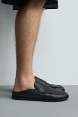 Mocasines destalonados de cuero color negro, de diseño liso con detalle de antifaz en el empeine y horma redonda.