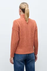 Polera de tejido de punto color ocre con cuello alto, diseño de rombos en relieve en el frente y mangas con detalle de trenzas laterales.