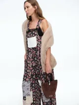 Mono de estilo jardinera con estampado floral y detalles de parches en diferentes texturas y patrones. Presenta un bolsillo frontal en color claro, tirantes ajustables con hebillas metálicas y piernas de corte recto y holgado.