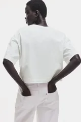 Remera blanca de corte cuadrado, con cuello redondo y mangas cortas.