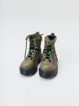 Botas de cuero estilo trekking, en combinación de colores verde, marrón y gris, con plataforma de goma negra, cordones bicolor inspirados en cuerdas de escalada y pasadores en tono rojizo.