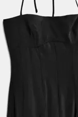 Vestido largo de color negro con cuello halter y escote recto. Presenta un diseño fluido con cierre de cremallera oculta en la espalda y lazada ajustable en el cuello.
