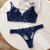 Conjunto de lencería azul con bordados florales transparentes, compuesto por un soutiene bralette de escote pronunciado y una bombacha cavada con tiras finas.