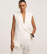 Chaleco largo de sastrería color blanco, con solapas tipo peaked, cierre frontal oculto y ajuste mediante lazo con hebilla en la espalda.