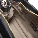 Cartera pequeña estructurada color negro, con material exterior símil gamuza y detalles en PU. Cuenta con cierre superior de cremallera metálica, doble asa fija de mano y correa larga regulable y desmontable. Presenta el logo XL en dorado en la parte frontal y herrajes metálicos dorados. Incluye un bolsillo interno con cierre.