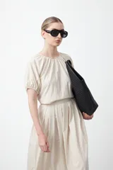 Top negro de manga corta con escote redondo y frunces en la costura de la sisa, creando un efecto de manga abullonada. El tejido parece ligero y con textura.