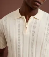 Camisa de punto color marrón con textura acanalada y perforaciones. Presenta cuello polo con cierre de cremallera frontal y mangas cortas.