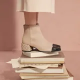 Botas cortas color beige con puntera negra charol y tacón bajo acolchado con diseño de rombos.