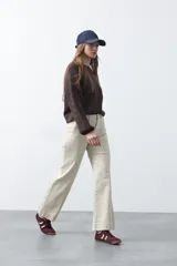 Pantalón de mujer color beige claro, de tiro alto, con corte recto y pierna ancha. Presenta costuras verticales marcadas en el frente de las piernas.