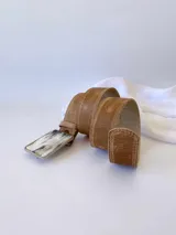 Cinto de cuero color camel con forro de cuero y hebilla rectangular de guampa con borde metálico trenzado. Cuenta con broche suizo intercambiable.