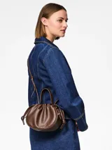 Bolso tipo saco o 'balloon' de efecto cuero color marrón oscuro (Chicory Coffee) con asa superior y correa ajustable para llevar al hombro o cruzado. Presenta herrajes plateados y cierre magnético.