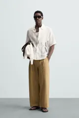 Camisa de calce relajado confeccionada en tejido ligero de lino y viscosa, con cuello solapa, manga corta y cierre frontal de botones. Presenta un diseño estampado de cactus en color gris en la parte inferior sobre un fondo blanco roto.