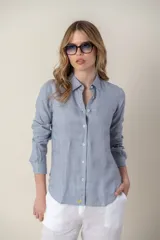 Camisa de lino color mostaza con cuello clásico, cierre frontal de botones y mangas largas con puños abotonados. Presenta un pequeño bordado distintivo en el ruedo inferior.