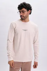 Remera manga larga de color beige, con cuello redondo y pequeña estampa de texto en el pecho.