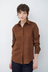 Camisa de estilo casual confeccionada en material tipo gamuza color marrón, con cuello clásico, cierre frontal con botones y costuras a la vista en tono contrastante.