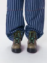 Botas de cuero estilo trekking, en combinación de colores verde, marrón y gris, con plataforma de goma negra, cordones bicolor inspirados en cuerdas de escalada y pasadores en tono rojizo.