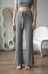 Pantalón tipo palazzo de tejido de punto acanalado en color gris, con cintura elástica y cordón ajustable. Presenta un corte recto y holgado con costuras verticales decorativas.