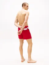 Short de baño rojo con cintura elástica ajustable con cordón, corte amplio y logo de Tommy Hilfiger en la pierna. Presenta una franja diagonal blanca con el logo de la marca en la parte inferior.