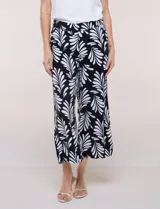 Pantalón crop de lino y rayón marca Dash, con estampado de hojas en blanco sobre fondo negro. Presenta tiro medio, pretina elástica en la parte trasera y bolsillos frontales.