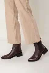 Bota tipo chelsea de caña media con acabado efecto cocodrilo en color chocolate. Presenta paneles elásticos laterales, puntera cuadrada y taco ancho geométrico.