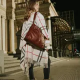 Poncho de tejido de punto con diseño de cuadros escoceses en tonos beige, negro y rojo. Presenta un corte amplio, cuello abierto y terminaciones con flecos en el ruedo.