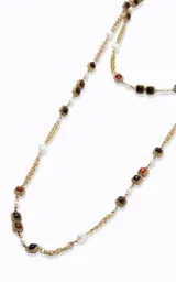 Collar largo de diseño en capas, elaborado en metal con acabado dorado. Presenta una estructura de cadena fina intercalada con aplicaciones de perlas blancas y piedras cuadradas en tonos rojizos y oscuros.