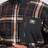 Campera de polar con cierre frontal completo y cuello alto. Presenta un diseño a cuadros en tonos oscuros con líneas rojas y blancas. Incluye un bolsillo frontal en el pecho con cierre y detalles en tela técnica negra.