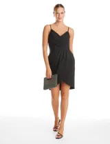Vestido corto de crepe color negro con escote en V cruzado y drapeado en el busto. Presenta una falda envolvente con diseño drapeado y abertura asimétrica en el bajo, con cierre invisible en la espalda y forro interno.