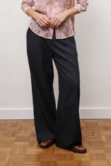 Pantalon de corte recto y pierna ancha, confeccionado en tejido tipo denim oscuro. Presenta tiro alto, cintura con cierre frontal y bolsillos laterales funcionales.