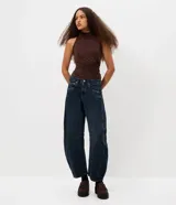 Pantalón de jean estilo baggy balloon, de tiro medio y corte amplio con diseño redondeado en las piernas. Presenta recortes laterales, cierre frontal con botón y cremallera, y bolsillos funcionales.