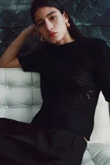 Top negro de manga corta en tejido de punto estilo crochet, con escote redondo, hombreras y cierre oculto en la espalda.