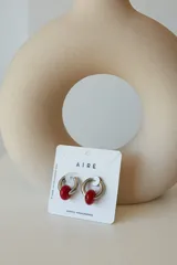 Aros tipo argolla de acero quirúrgico plateado con un dije de piedra natural esférica en color rojo.