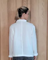 Camisa de manga larga con estampado de rayas verticales en tonos crudo y beige. Presenta cuello alto con volados, cierre frontal con botones dobles y puños con volados.