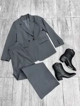 Conjunto sastrero de color gris, compuesto por un blazer oversize de doble botonadura con bolsillos con solapa y un pantalón de corte recto y pinzas en la parte delantera.