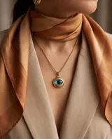 Collar de bronce dorado con cadena fina y dije redondo en relieve con diseño de ojo turco esmaltado en tonos azul y negro.
